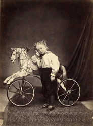 Niño pequeño junto a su caballo montado como un triciclo, 1860s